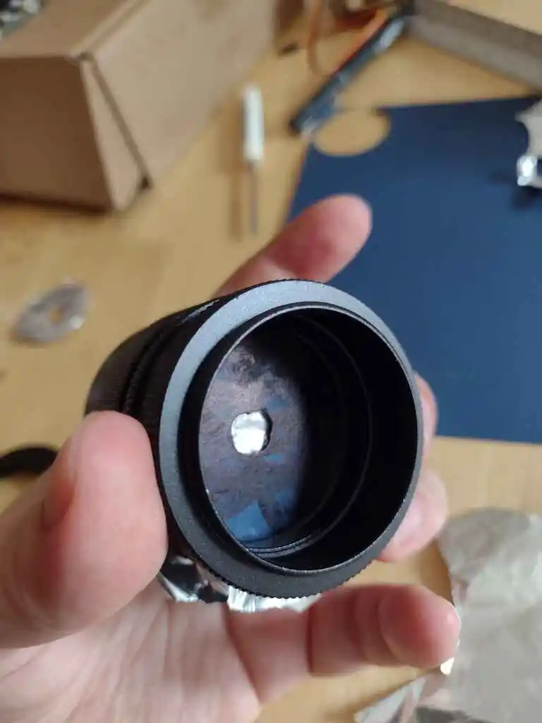 picture of camera lens with tinfoil covering aperture behind bored hole