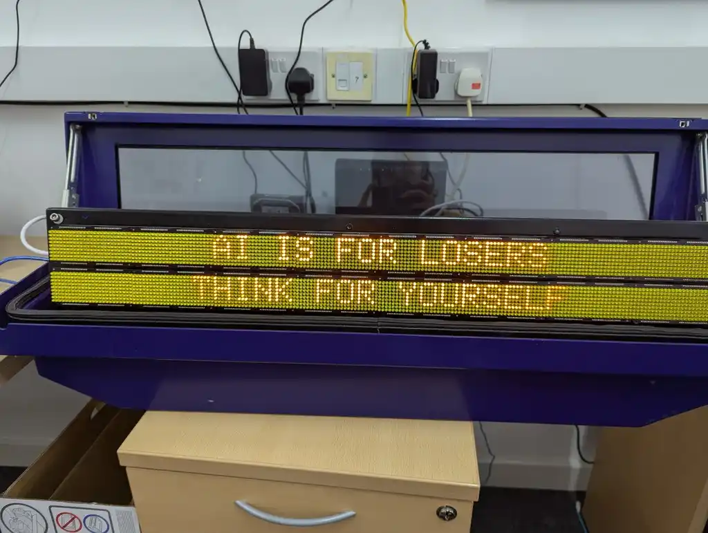 picture of LED bus sign displaying text "AI IS FOR LOSERS" "THINK FOR YOURSELF"