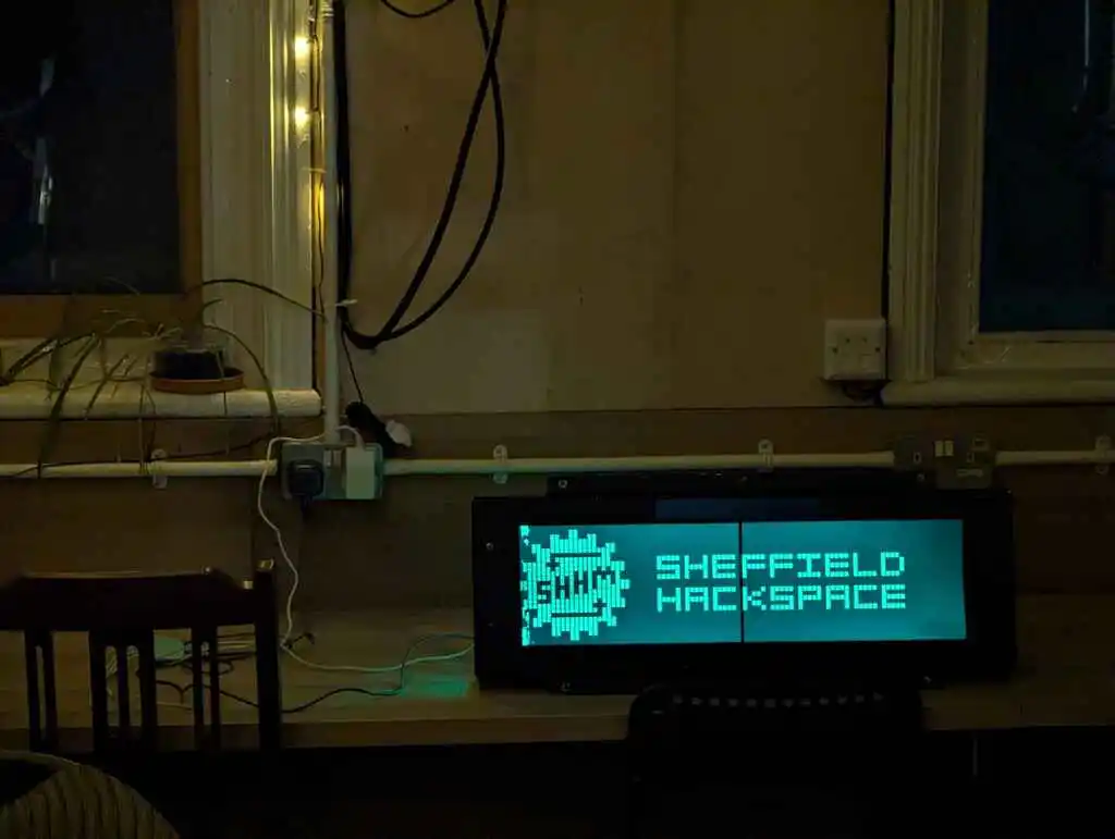 picture of large LCD train sign displaying hackspace logo in the dark