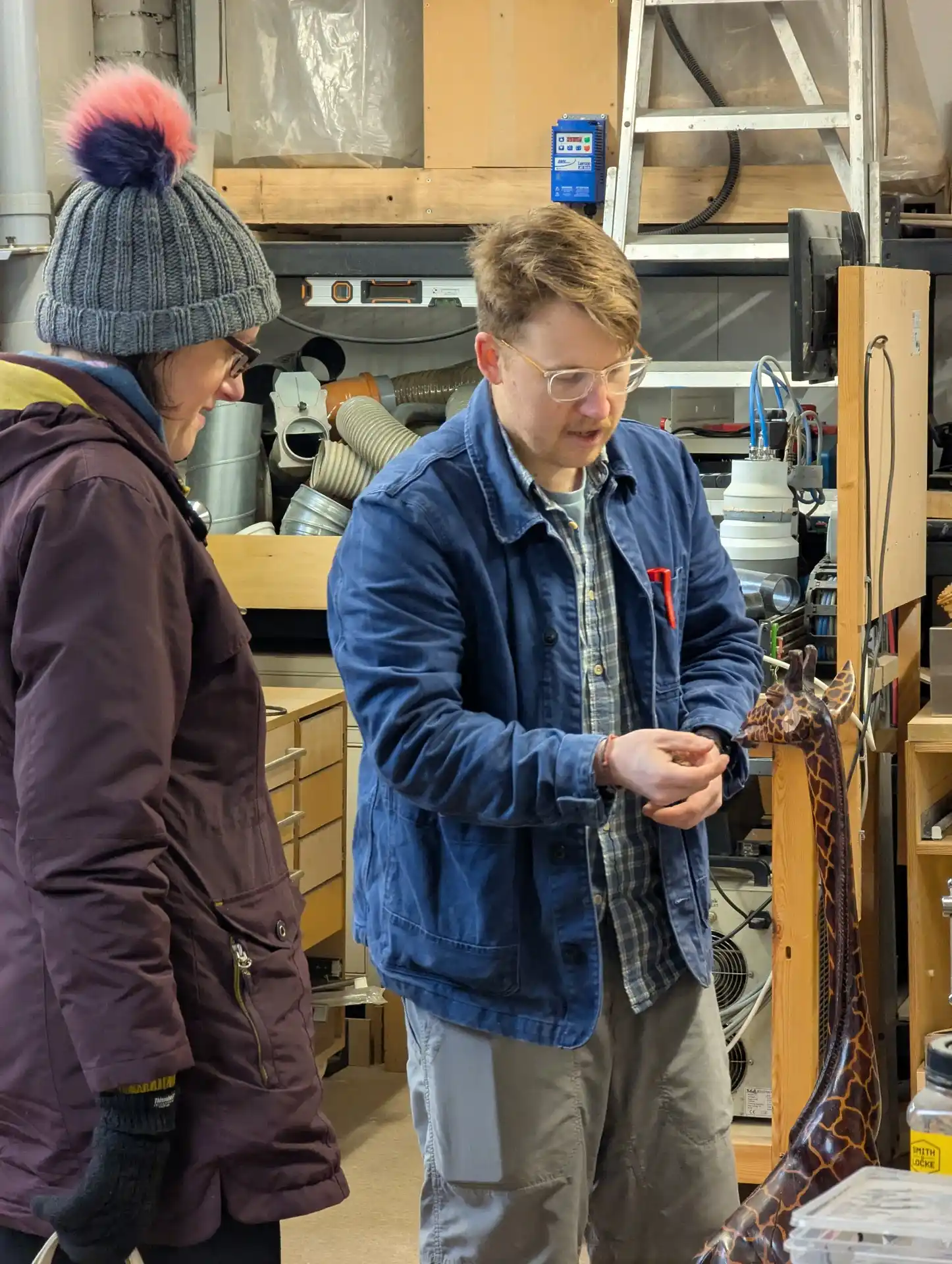 picture of two people looking at a repair on a wooden giraffe